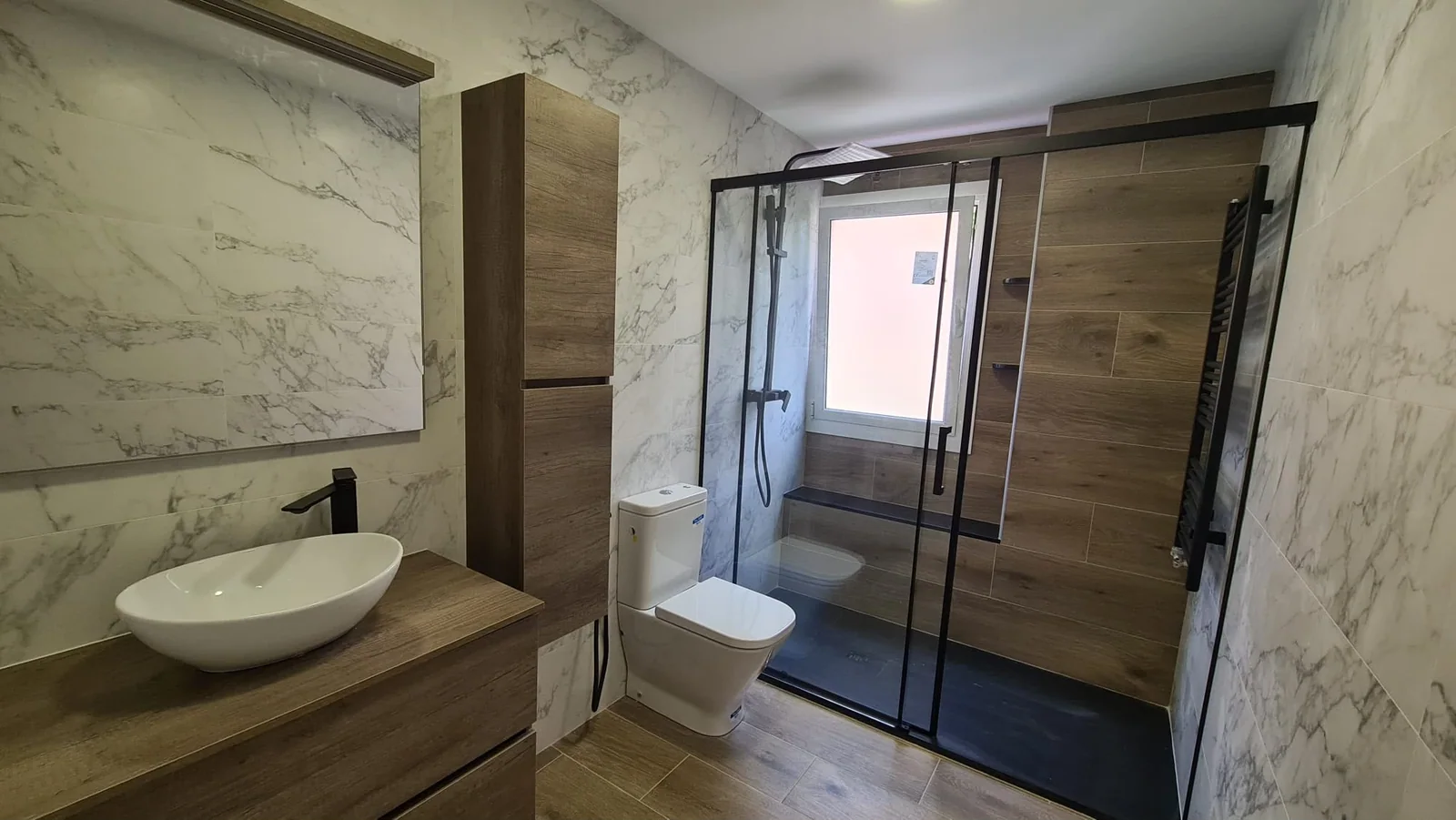 Baño de Grupo Diper con mueble de madera, lavabo sobre encimera y mampara negra