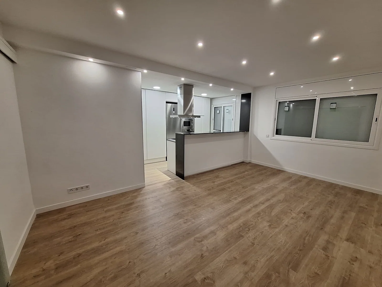 Interior terminado con suelo de madera, paredes blancas y cocina abierta con península